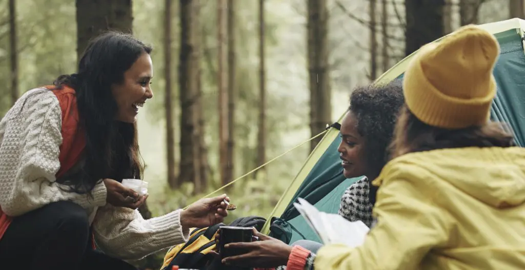 Three adult women on a camping trip make coffee near a tent