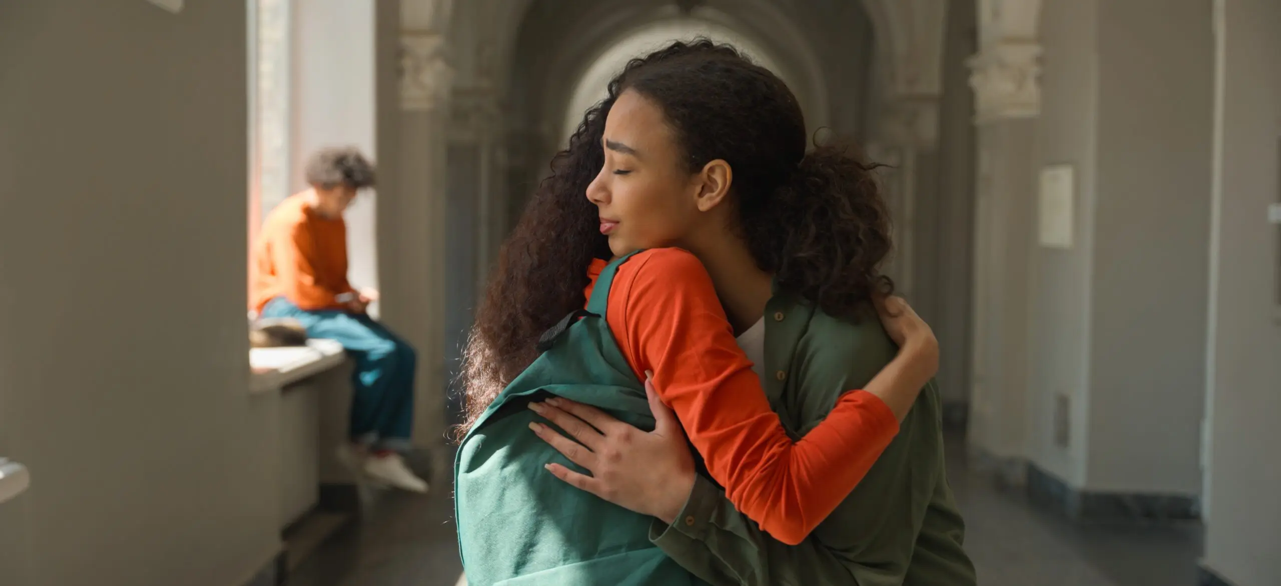 A pair of teenage girls hugging, one with a sympathetic expression on her face