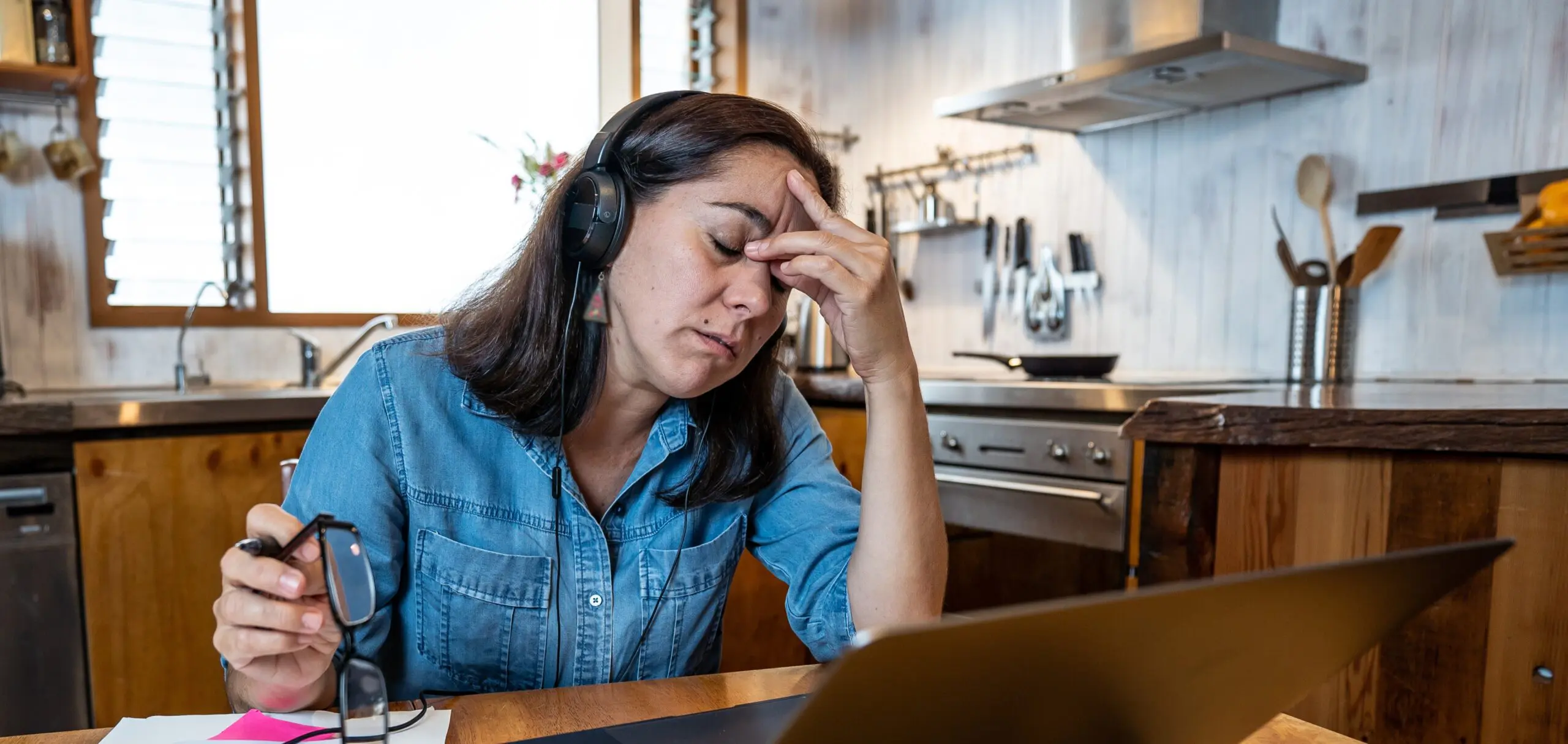 A woman sits in front of a computer, stressed and pinching the bridge of her nose