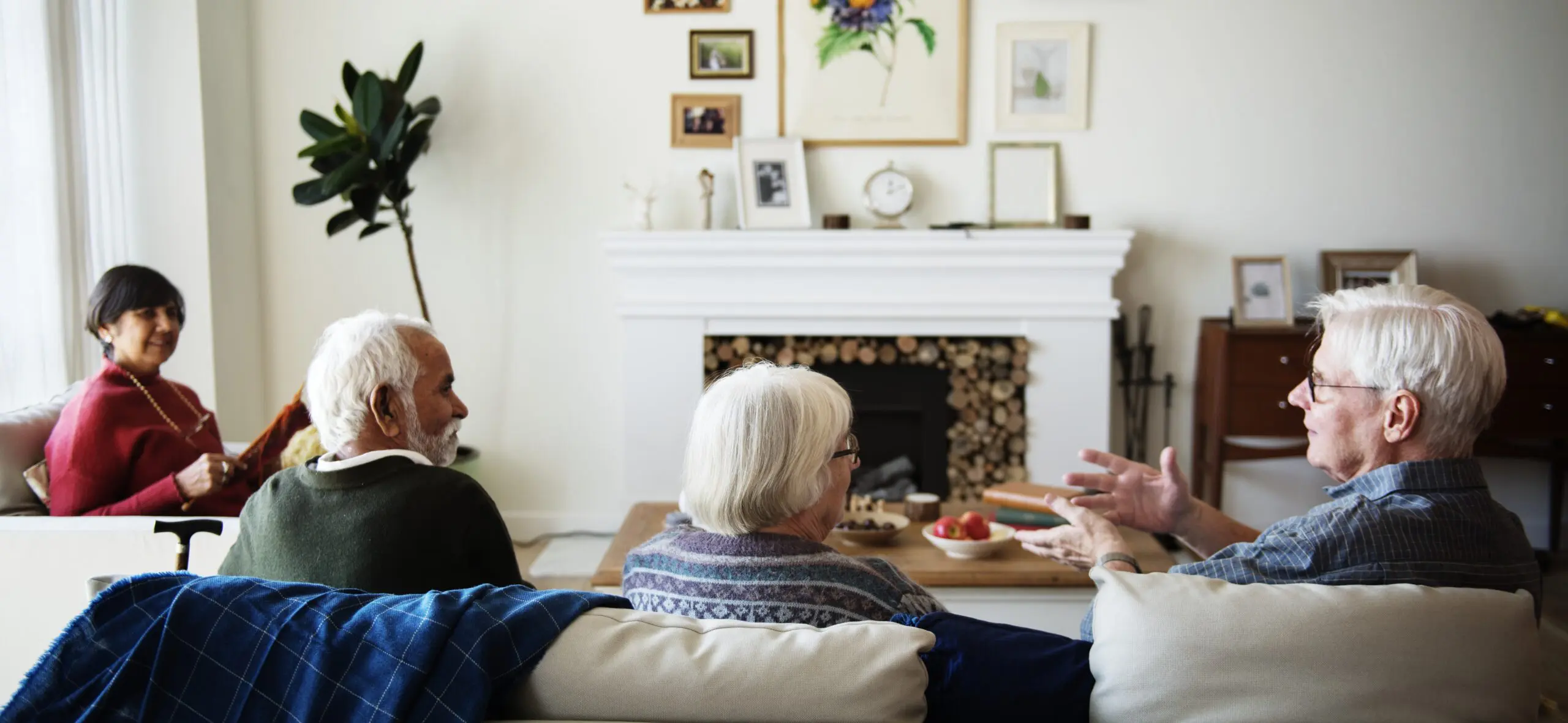 A group of older friends sit in a living room facing each other and communicating