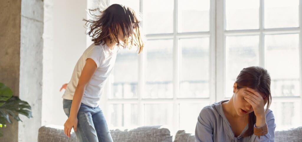 child jumping on couch with upset mother sitting next to her