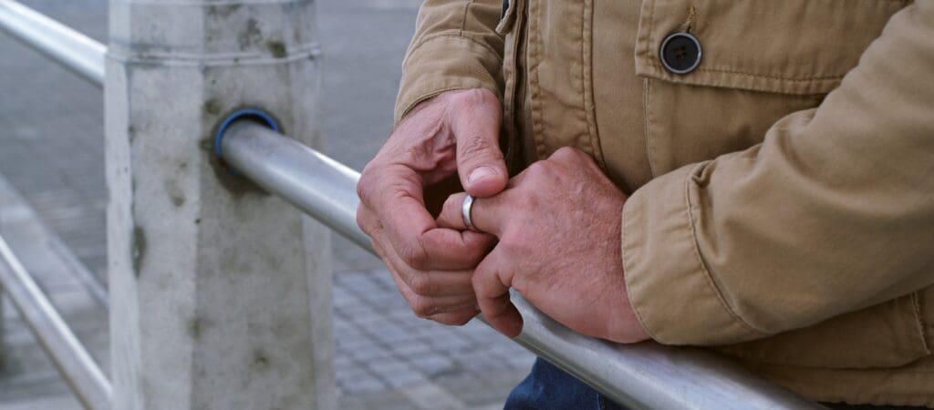 A set of male hands rests on a railing as the man adjusts his wedding ring