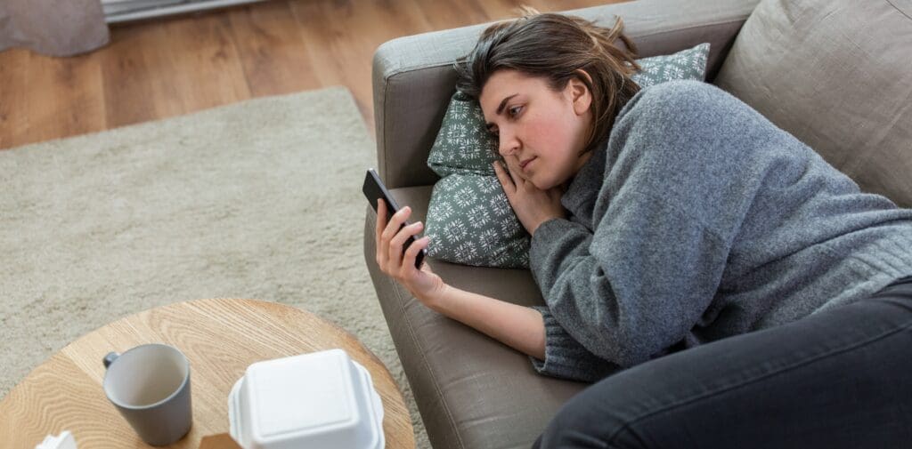A woman lays on her couch staring blankly at her phone
