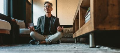 A man sits next to his coffee table, eyes closed and meditating
