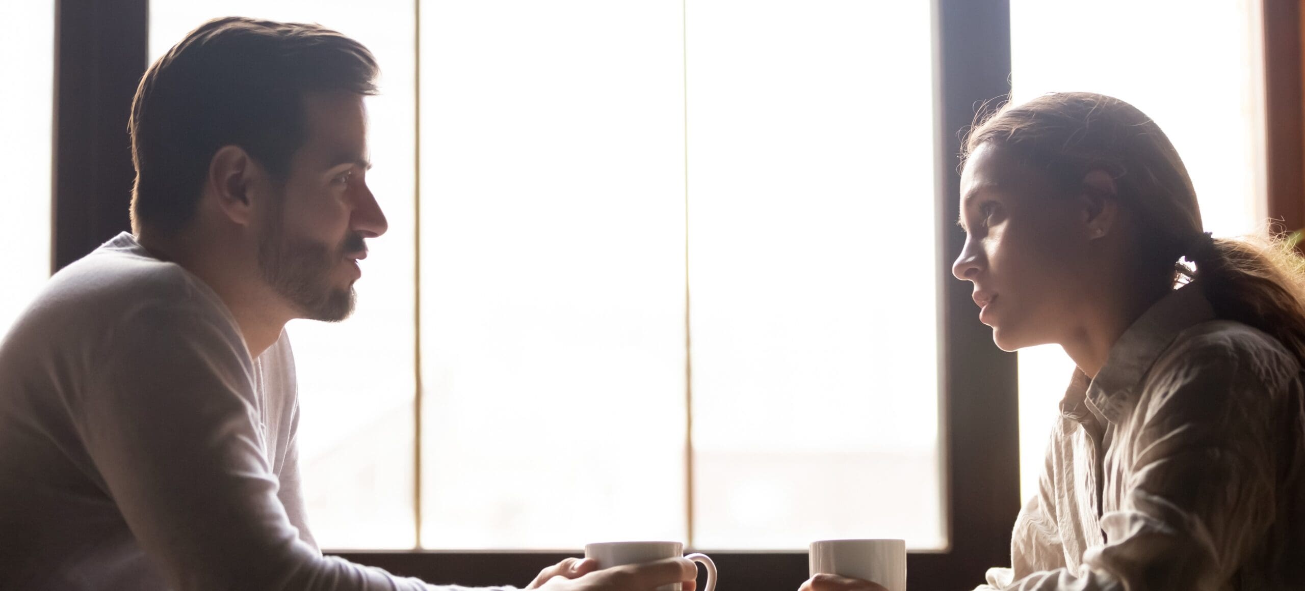 A couple sits across from each other at a coffee table talking directly and thoughtfully