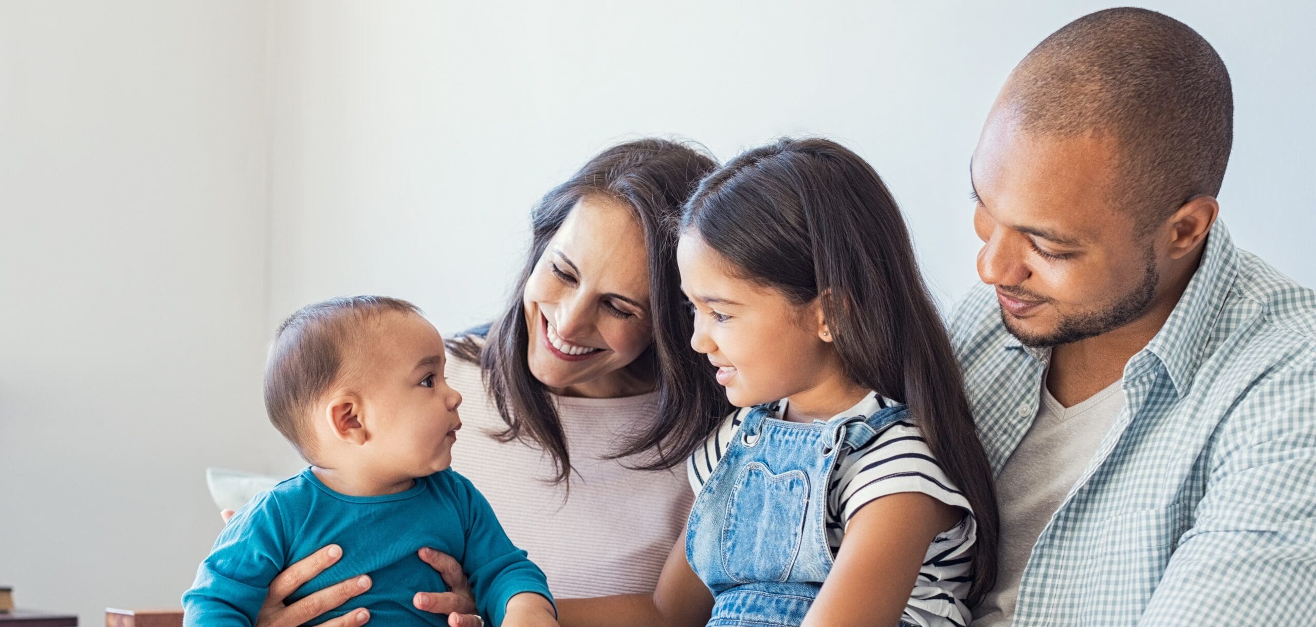 A family with two young children sit in a clump with the youngest looking back at everyone smiling