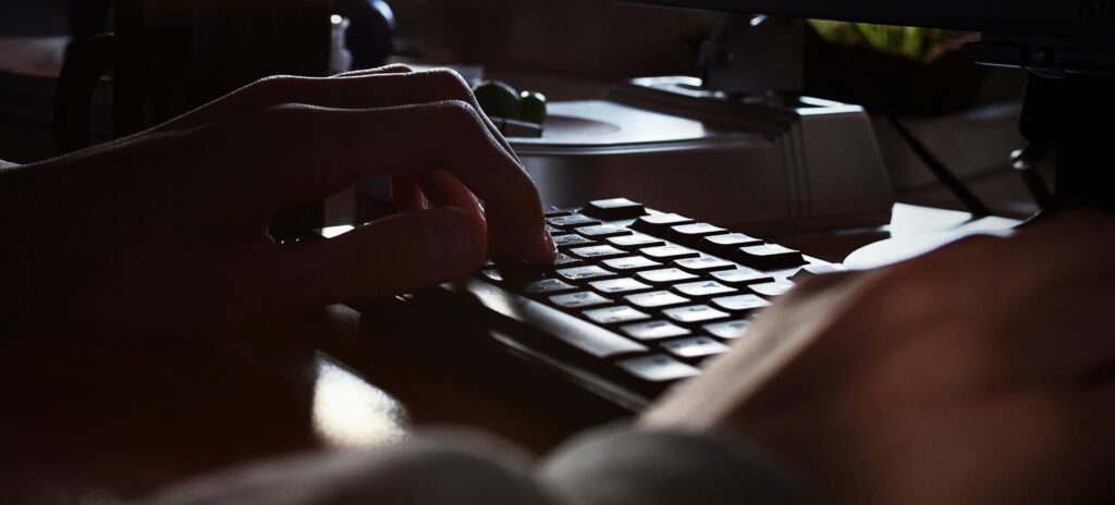 A set of unidentifiable hands rests on a computer keyboard
