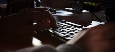 A set of unidentifiable hands rests on a computer keyboard