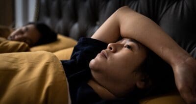 A woman lays in bed with her arm thrown over her eyes thinking
