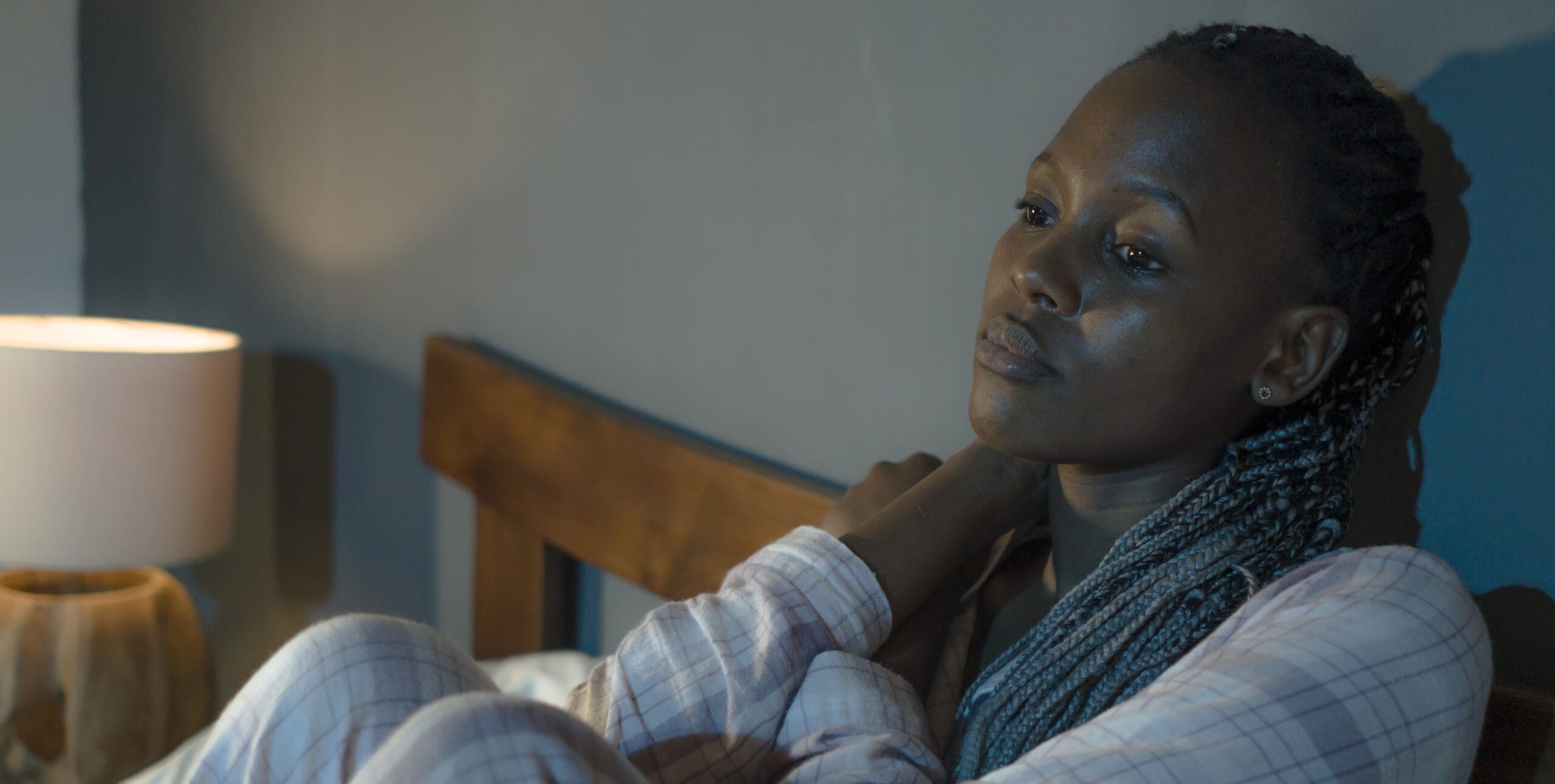 A woman leans against her headboard, frustrated and unable to sleep