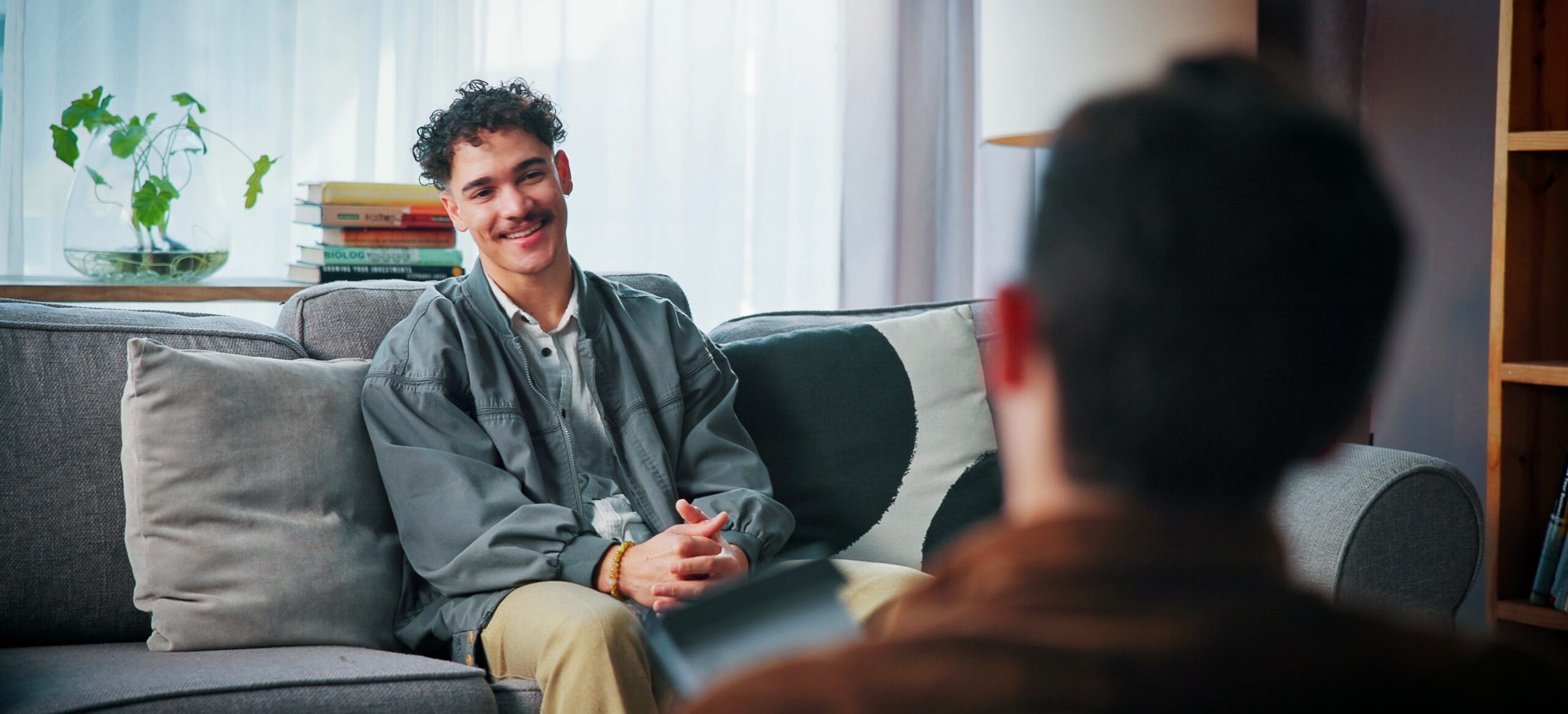 A young man sits on a couch talking to a therapist and looking hopeful