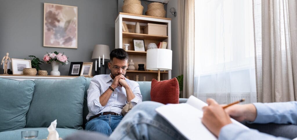 A man sits on a therapist couch looking lost in thought