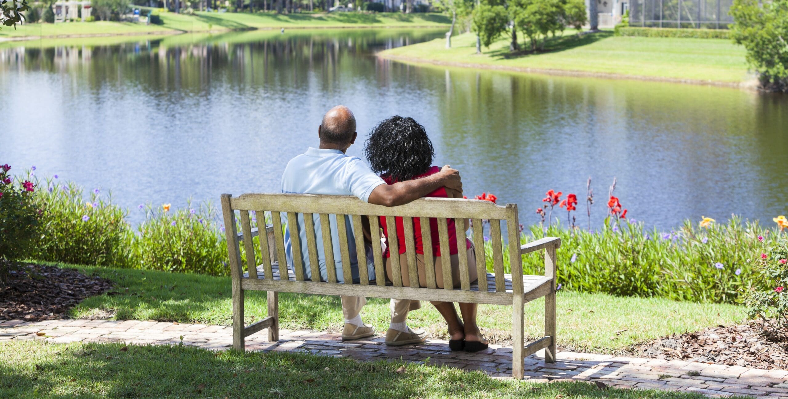 A couple sits on a bench facing a lake, content and leaning on each other