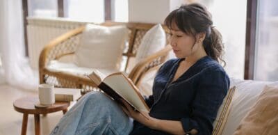 A woman sits on her couch contentedly reading her book